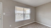 This single-floor, 2-bedroom, 1-bathroom home offers a practical and efficient layout designed to maximize every square foot of its cozy footprint. The living room greets residents at the entrance, featuring neutral taupe walls, light tile flooring, and a large window fitted with horizontal blinds that allow ample natural light to filter in. The combined kitchen and dining area is well-appointed with a galley-style kitchen featuring ample cabinetry, light countertops, a full suite of white appliances including an electric range, refrigerator, and dishwasher, all set over easy-to-clean tile flooring. A chandelier overhead adds a touch of character to the dining space. The spacious primary bedroom is carpeted for comfort, finished in neutral tones, and connects to a dedicated closet outfitted with built-in shelving and hanging rods for organized storage. The second bedroom, also carpeted, includes a window with natural views and a closet. The full bathroom is clean and functional, featuring a wide vanity with generous counter space, a large mirror, under-sink cabinetry, and a tiled shower-tub combo. Consistent neutral paint tones, white trim, and tile flooring throughout the common areas create a cohesive and move-in-ready atmosphere.
