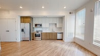 Located along Buchtel Boulevard in Denver, CO, this single-floor residence offers a clean, contemporary design with an open layout and modern finishes throughout. Light hardwood-style flooring runs seamlessly across the living, bedroom, and kitchen areas, creating a warm and cohesive aesthetic.

The kitchen is a standout feature, outfitted with a full suite of stainless steel appliances including a French door refrigerator, electric range, over-the-range microwave, and dishwasher. Two-tone cabinetry pairs light upper cabinets with wood-grain lower cabinets beneath a bright, horizontal tile backsplash and clean white countertops, delivering both style and function. Recessed lighting enhances the kitchen's polished look.

The bedroom is bathed in natural light through multiple large windows fitted with horizontal blinds, complemented by a ceiling fan for added comfort. The open doorway between the bedroom and living area promotes a sense of flow and connectivity throughout the unit.

The bathroom features large-format marble-look tile flooring, a wood-grain vanity with a white countertop, and a beautifully tiled walk-in shower. The clean white walls and minimalist design give the bathroom a bright, spa-like quality. Overall, this residence combines modern design with practical finishes in a well-located Denver neighborhood.