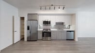 Located at 1105 E Katella Ave in Anaheim, California, this single-floor residence offers a well-designed layout with modern finishes throughout. The kitchen is a standout feature, outfitted with stainless steel appliances including a side-by-side refrigerator with ice and water dispenser, a gas range with oven, built-in microwave, and dishwasher. Cabinetry combines white upper cabinets with wood-toned lower cabinets, complemented by a grey subway tile backsplash and light quartz countertops. Track lighting above the kitchen provides ample illumination, while light wood-look flooring extends through the main living areas, creating a bright and cohesive aesthetic. A dedicated pantry closet adjacent to the kitchen offers generous additional storage. The bedrooms feature soft carpeting and windows dressed with horizontal blinds, allowing for natural light and privacy. In-unit laundry is conveniently housed behind a louvered door, featuring a stacked washer and dryer. The bathroom is finished with wood-look tile flooring, a single-sink vanity with wood-toned cabinetry, built-in wall shelving, and a full soaking tub with shower combination. Clean, neutral walls throughout lend the space a fresh and move-in-ready feel.
