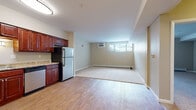 Located at 1800 Silas Deane Highway in Rocky Hill, Connecticut, this single-floor unit offers a practical and functional layout with a seamless flow between its main living areas. The kitchen is a standout feature, outfitted with rich cherry wood cabinetry, granite-style countertops, and a full suite of stainless steel appliances including an electric range, dishwasher, and refrigerator. Durable hardwood-style flooring runs throughout the kitchen and entryway, providing a clean and easy-to-maintain surface. The open living and dining area transitions naturally from the kitchen, featuring plush carpeting that adds warmth and comfort underfoot. Natural light filters in through horizontal windows, complemented by wall-mounted air conditioning and baseboard heating units to ensure year-round climate control. A spacious bedroom is finished with soft carpeting, neutral-toned walls, and its own baseboard heating. The bathroom includes a full-size soaking tub with a shower, hardwood-style flooring, and a grab bar for added accessibility. Additional storage is provided by a set of double closet doors near the entry. The overall aesthetic is clean and neutral, offering a move-in-ready space suited for comfortable everyday living.