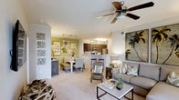 Located at 1431 W Nine Mile Rd in Pensacola, Florida, this single-story residence offers a thoughtfully designed open-concept floor plan that seamlessly connects the living, dining, and kitchen areas into one cohesive and welcoming space. The living area is anchored by plush carpeting and a ceiling fan with integrated lighting, creating a comfortable and well-ventilated atmosphere. Coastal-inspired artwork and lush green accent walls add a vibrant, relaxed character throughout the space. The kitchen features dark cabinetry, a breakfast bar with counter seating, and stainless steel appliances, making it both functional and stylish. It opens directly to the dining area, which is framed by decorative wall art and a track lighting fixture, lending warmth and charm to mealtimes. A partial decorative column subtly defines the boundary between the dining and living spaces while maintaining an airy, open feel. Crown molding along the ceilings adds a refined architectural touch throughout. The overall ambiance is bright, inviting, and cohesive, with a coastal Florida aesthetic running throughout the design. This well-appointed single-floor layout is ideal for comfortable everyday living and entertaining.