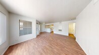 Located at 3651 N Rancho Dr in Las Vegas, NV, this single-floor residence offers three bedrooms and two bathrooms across a well-organized layout. The open-concept living and dining area is a standout feature, showcasing warm wood-look flooring, a textured ceiling, and large windows dressed with vertical blinds that allow ample natural light to fill the space. The kitchen is positioned at the heart of the home, featuring a convenient peninsula with counter seating, white cabinetry, a full suite of white appliances including a refrigerator and electric range, and a bright overhead light panel that adds a warm glow. The spacious primary bedroom includes a closet and exterior-facing windows with outdoor views. The additional bedrooms are well-proportioned, each with wood-look flooring and windows that bring in natural light. Both bathrooms are finished consistently with white cabinetry, granite-style countertops, a single vanity sink, and a full tub-shower combination with white tile surround. Wood-look flooring carries throughout the bathrooms as well, maintaining a cohesive aesthetic. A hallway connects the private areas of the home, and the overall design emphasizes a clean, neutral palette throughout.