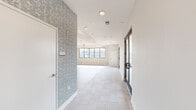 Located at 501 4th Ave SE in the heart of Cedar Rapids, Iowa, this thoughtfully designed single-floor space combines modern aesthetics with functional versatility. The open-plan interior is finished with light hardwood-style flooring throughout much of the space, complemented by large-format tile in key areas. A striking feature wall adorned with a soft botanical-patterned wallcovering adds texture and character, creating a refined focal point against the otherwise clean, neutral palette.

The main living and entertaining area is anchored by a tray ceiling with a contemporary multi-arm chandelier, while recessed lighting provides consistent illumination throughout. A peninsula-style counter with pendant lighting above defines a kitchenette zone, accompanied by white cabinetry and built-in storage. Black-framed windows and French doors frame sweeping views of the Cedar Rapids skyline, flooding the interior with abundant natural light.

A dedicated built-in credenza with cabinetry sits beneath an additional wallpapered accent wall, offering both style and practicality. The space also features direct access to a generously sized outdoor rooftop terrace, finished with large-format pavers and a partially covered overhang with a warm wood-paneled ceiling — perfect for enjoying open-air city views.