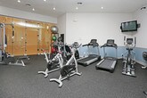 This state-of-the-art fitness center boasts a thoughtfully designed open-concept layout, maximizing space efficiency and functionality. The facility features a high ceiling with recessed lighting, creating a bright and energizing atmosphere. The flooring appears to be a durable, non-slip material suitable for various workout activities.

The space is well-equipped with a comprehensive range of exercise equipment. In the foreground, a Smith machine takes center stage, ideal for weight training and strength exercises. Behind it, a row of cardio machines, including treadmills, can be seen. The center area hosts various strength training equipment and free weights.

Along one wall, vibrant yellow lockers provide secure storage for personal belongings, adding a pop of color to the predominantly white and gray color scheme. Large mirrors line the walls, allowing users to monitor their form during workouts.

The gym's design emphasizes cleanliness and organization, with clearly defined zones for different types of exercises. This layout promotes easy navigation and efficient use of the space, catering to a variety of fitness preferences and goals. The overall ambiance suggests a modern, professional environment dedicated to health and wellness.