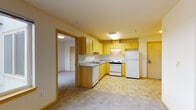 Located on the sixth floor at 12740 30th Avenue NE in Seattle's Lake City neighborhood, Unit 612 is a well-organized single-floor residence with a practical and comfortable layout. The kitchen is outfitted with light maple cabinetry offering generous storage, gray laminate countertops, a double sink, a coil electric range, dishwasher, and a full-size refrigerator. Tile flooring runs through the kitchen and entry areas, providing durability in high-traffic zones. The open living and dining area transitions seamlessly from the kitchen, featuring neutral carpet and easy access to the main entry door. Two bedrooms are carpeted and each includes a built-in closet with wire shelving for organized storage. The primary bedroom benefits from a large window that brings in natural light and offers views of the surrounding Seattle landscape, along with a baseboard heater for year-round comfort. The bathroom features tile flooring, a wood-toned vanity with a granite-style countertop, a wide wall mirror with overhead lighting, and clean, neutral finishes throughout. The unit's overall palette of warm neutrals and natural wood tones creates a calm and cohesive atmosphere throughout the space.