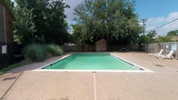 This single-story property combines curated interior design with functional outdoor amenities. The exterior features a generously sized rectangular swimming pool with a teal-tinted finish, surrounded by a concrete deck and enclosed by a wooden privacy fence. Mature trees provide natural shade, and a storage shed is positioned at the rear of the yard, adding practical utility to the outdoor space.

Inside, the interior walls display a lightly textured finish in a neutral white tone, creating a clean and understated backdrop that complements the overall aesthetic. Recessed lighting illuminates the spaces efficiently throughout. The dining area serves as a notable focal point, centered around a substantial round green marble pedestal table paired with woven rattan-style chairs atop a woven area rug. A large framed abstract artwork anchors one wall, contributing an artistic element to the room. Dark stained concrete flooring runs throughout, providing an industrial yet refined character.

A distinctive sliding barn door opens to an adjacent space, while a set of aged, distressed French-style doors adds architectural contrast and visual interest. The flow between rooms feels open and connected, reinforcing the cohesive, design-forward nature of the space.