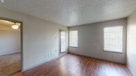 This single-floor unit offers a practical and well-organized layout across several distinct areas. The living space is bright and open, featuring rich wood-style flooring that extends throughout the main areas. Multiple windows fitted with horizontal blinds allow natural light to filter in, creating a welcoming atmosphere. A panel-style front door provides direct access to the living area.

The kitchen is a functional galley-style space equipped with dark espresso cabinetry, dark granite-style countertops, a mosaic tile backsplash, and black appliances including a refrigerator, range, and built-in microwave. A peninsula counter with an overhang separates the kitchen from the adjacent living and dining areas, providing additional workspace and casual seating potential.

The bedroom features plush wall-to-wall carpeting and a centered ceiling light fixture, with a window offering natural light. The bathroom includes a full tub and shower combination with white tile surround and wood-style flooring. Throughout the unit, textured walls and popcorn ceilings are consistent design elements. Ceiling vents provide climate control throughout the space.