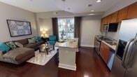 Located in the heart of downtown Raleigh, NC, this well-appointed one-bedroom residence offers a thoughtfully designed single-floor layout that balances contemporary style with everyday functionality. The open-concept living and kitchen area serves as the centerpiece of the home, anchored by rich dark hardwood flooring that flows throughout. The kitchen is equipped with stainless steel appliances — including a range, microwave, dishwasher, and French door refrigerator — complemented by warm-toned wood cabinetry and granite countertops. A granite-topped island with pendant lighting above provides additional prep space and serves as a natural dining area. The living room offers generous space for relaxing and entertaining, with access to a private balcony overlooking an outdoor amenity area. The bedroom features plush carpeting, a dedicated walk-in closet with built-in shelving, and a calm, neutral color palette. The bathroom includes a granite-topped vanity with wood cabinetry, tile flooring, and a tub-shower combination. A hallway with decorative wall accents connects the living and sleeping areas with purpose and style. Throughout the residence, neutral tones and modern finishes create a cohesive and inviting ambiance.