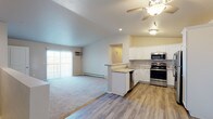 This single-floor residence offers a thoughtfully designed open-concept layout that seamlessly connects the kitchen and living area. The kitchen is well-equipped with stainless steel appliances, including a refrigerator, range, microwave, and dishwasher, complemented by crisp white cabinetry, granite-style countertops, and durable wood-look flooring. A peninsula with a sink serves as a natural divider between the kitchen and the carpeted living area, which features a ceiling fan and a sliding glass door that invites natural light. Two bedrooms are generously sized, each with plush carpet, ceiling fans, baseboard heating, and ample closet space. One bedroom also includes a wall-mounted air conditioning unit. The two bathrooms are finished consistently with the rest of the home, featuring white vanities with granite-style countertops and wood-look flooring. One bathroom includes a walk-in shower, while the other offers additional storage cabinetry. A dedicated laundry room houses a full-size washer and dryer alongside a water heater. The overall ambiance is clean, bright, and move-in ready, with a cohesive modern aesthetic carried throughout every room.