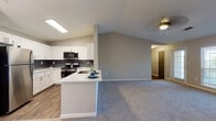 Located at 3315 Preston Pointe Way in Cumming, Georgia, this single-floor residence offers a thoughtfully designed open-concept layout that maximizes comfort and functionality. The living area is highlighted by soaring vaulted ceilings and a ceiling fan, creating an airy, spacious atmosphere. A classic white-mantled fireplace serves as a focal point, complemented by large windows that allow generous natural light to fill the room. Plush carpeting throughout the living and bedroom spaces adds warmth and comfort.

The kitchen is well-equipped with white shaker-style cabinetry, stainless steel appliances including a refrigerator, range, and over-the-range microwave, and a dark subway tile backsplash that provides a modern contrast. A peninsula with a white countertop and integrated sink offers additional prep space and casual seating. Wood-look flooring anchors the kitchen area seamlessly.

The bedrooms are generously sized, each featuring ceiling fans, plush carpeting, and ample natural light from well-placed windows. The primary bedroom includes direct access to an en-suite bathroom. Both bathrooms are finished with white vanities, framed mirrors, and wood-look tile flooring, with tub-shower combinations providing clean, functional design throughout.