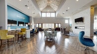 Located at 2100 Haddonfield Road in Pennsauken, NJ, the Haddon Point community clubhouse is a thoughtfully designed single-floor amenity space that makes a striking first impression. The centerpiece of the building is a grand, open lounge anchored by soaring vaulted ceilings clad in wood paneling, with clerestory windows that flood the interior with natural light. Rich herringbone-patterned hardwood floors run throughout, complementing a palette of teal, gold, and gray tones that define the space's modern coastal aesthetic. A bold teal feature wall bearing the Haddon Point branding serves as a focal point, backed by a long white bar-height counter with stylish seating — ideal for social gatherings or leasing activities. Multiple seating arrangements offer flexible use, from intimate lounge clusters with plush upholstered chairs to casual conversation areas. A dedicated lounge nook features a white brick fireplace wall with a mounted television and striking blue velvet accent chairs. The game room stands out with a coffered ceiling, pool table, shuffleboard, and a large chalkboard mural. Throughout the space, plantation shutters frame views of the surrounding community, while pendant lighting and a sputnik chandelier add elegant finishing touches.