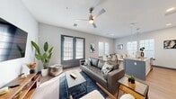 This well-designed single-floor residence showcases a contemporary open-concept layout that seamlessly connects the living, dining, and kitchen areas. The living room is anchored by a tufted leather sofa, a ceiling fan, and light wood-style flooring, with natural light streaming in through multiple windows fitted with plantation shutters. A set of charcoal-framed French doors adds a stylish touch and opens the space further.

The kitchen is outfitted with stainless steel appliances, white cabinetry, granite countertops, pendant lighting, and a peninsula with bar seating — ideal for casual dining or entertaining. Adjacent to the kitchen, the dedicated dining area features large windows on two walls, flooding the space with abundant natural light.

The bedroom is a comfortable retreat with plush carpeting, generous natural light, teal accent curtains, and access to a well-organized walk-in closet with built-in shelving. The bathroom features a granite-topped vanity with white cabinetry, a large mirror, a combination tub and shower, and a bright window that enhances the clean, neutral aesthetic. Throughout the space, a consistent cool-toned color palette and modern finishes contribute to a cohesive, polished ambiance.