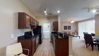 This single-floor residence offers a thoughtfully designed open-concept layout that seamlessly connects the kitchen, dining, and living areas. The kitchen is a standout feature, showcasing rich dark wood cabinetry, sleek dark granite countertops, and black appliances, including a range, refrigerator, and dishwasher. Track lighting illuminates the galley-style workspace, while a peninsula counter provides a natural transition into the dining and living spaces. Conveniently, an in-unit washer is tucked just off the kitchen corridor. The living room is bright and welcoming, anchored by a ceiling fan and filled with natural light through large sliding glass doors that open to a private patio with outdoor seating and green views beyond. The bedroom features plush carpeting and direct access to a full bathroom appointed with dark granite countertops, rich wood vanity cabinetry, a tiled tub-shower combination, and tile flooring. A second bathroom mirrors the same finishes. An additional flex room with a large window offers versatility as a home office or secondary bedroom. Throughout the space, warm neutral tones, wood-look flooring in the main areas, and carpet in the living and sleeping spaces create a cohesive and comfortable atmosphere.