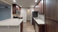 The Griffith Downstairs is a well-appointed 2-bedroom, 2-bathroom single-floor residence designed with both comfort and functionality in mind. The kitchen serves as a central highlight, featuring rich dark-wood cabinetry, granite countertops, stainless steel appliances including a refrigerator, electric range, and built-in microwave, recessed lighting, and wood-look tile flooring. A kitchen island provides additional prep and counter space, making it ideal for everyday cooking and entertaining.

Both bedrooms are generously sized, carpeted, and filled with natural light through large windows fitted with horizontal blinds. The primary bedroom benefits from a spacious walk-in closet outfitted with multiple shelving units and double hanging rods, offering excellent organizational capacity.

The two bathrooms are identically appointed, each featuring a tub/shower combo, a vessel sink atop a granite-topped dark vanity, wood-look tile flooring, and brushed nickel fixtures and hardware — delivering a cohesive, modern aesthetic.

A dedicated in-unit laundry area houses a full-size top-load washer with overhead shelving for storage. The overall design palette of warm neutrals, quality finishes, and durable materials creates a clean, move-in-ready living environment throughout the entire residence.