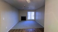 This single-story space features a living area that combines functional design with comfortable details. The room is anchored by a tile-surround fireplace, providing a focal point along one wall and adding a classic, cozy element to the space. A ceiling fan is installed overhead, contributing to air circulation and comfort throughout the room.

The flooring transitions between two materials: hardwood near the entryway and carpet covering the main living area, offering both durability and comfort underfoot. The textured ceiling adds subtle visual interest, while neutral-toned walls provide a versatile backdrop suitable for a variety of décor styles.

Natural light enters through a window dressed with vertical blinds, which allows for adjustable light control. The window also provides a view to the exterior. Baseboards are present throughout, lending a clean, finished look to the lower edges of the walls. The overall layout feels open and practical, making the living area well-suited for everyday use. The combination of the fireplace, mixed flooring, and natural light gives the space a straightforward yet inviting ambiance.