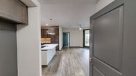 This thoughtfully designed 2-bedroom, 3-bathroom single-story residence offers a seamless blend of modern style and functional living. The open-concept kitchen and living area serves as the heart of the home, featuring rich dark-stained cabinetry, a striking marble-look quartz island with an undermount sink, stainless steel appliances, a textured tile backsplash, and pendant lighting overhead. Wood-look flooring runs throughout the main living areas, complemented by a ceiling fan and direct access to a covered balcony that overlooks lush greenery. The primary bedroom is generously sized with plush carpeting, large windows, and access to a walk-in closet outfitted with built-in shelving and hanging storage. The primary bathroom includes a wide vanity with marble-look countertops, a large framed mirror, and a glass-enclosed walk-in shower with tile surround. The second bedroom also features wood-look flooring and is served by its own bathroom. A dedicated laundry room houses a full-size front-loading washer and dryer beneath a granite-style folding counter. Neutral tones, dark accent trim, and consistent high-quality finishes create a cohesive, modern aesthetic throughout the entire residence.