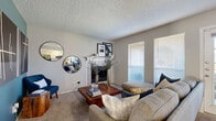 This thoughtfully designed single-floor, one-bedroom, one-bathroom residence offers a comfortable and functional layout across a compact yet efficient footprint. The open living room serves as the heart of the home, featuring plush carpet flooring, a textured ceiling, and a white-mantled fireplace that provides a warm focal point. Natural light enters through a large window fitted with blinds, brightening the neutral-toned walls throughout.

Adjacent to the living area, the galley-style kitchen is well-equipped with white cabinetry, granite countertops, stainless steel appliances, and hardwood-style flooring. A breakfast bar provides additional prep and dining space, while a separate dining nook — painted in a bold teal accent — comfortably seats four and features a window with outdoor views.

The bedroom is a serene retreat, highlighted by a striking teal accent wall, carpeted floors, a window for natural light, and access to a spacious walk-in closet outfitted with multi-level shelving and hanging rods. The bathroom includes a vanity with gray cabinetry and granite-style countertops, a tub-shower combination with tile surround, and hardwood-style flooring, completing this efficient and well-finished residence.