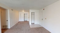 This well-appointed two-bedroom, two-bathroom residence offers comfortable single-floor living across a generous and efficiently designed layout. The living area features plush wall-to-wall carpeting and a ceiling fan, creating a relaxed atmosphere, while a sliding glass door with vertical blinds allows natural light to fill the space and provides direct access to the exterior. The galley-style kitchen is lined with ample white cabinetry, offering generous storage and counter space, complemented by tile flooring and white appliances including a full-size refrigerator. The entry area transitions seamlessly from tile to carpet, and the foyer features a coat closet for added convenience. Both bedrooms are carpeted and well-sized, each equipped with ceiling fans. The primary bedroom benefits from dual closets, including a walk-in, providing excellent storage capacity. Both bathrooms are identically appointed with a tub-shower combination set within an arched alcove, a wood-vanity with a single sink, a mirror with overhead lighting, and tile flooring — offering a clean, functional design. Throughout the unit, the neutral color palette and consistent finishes create a cohesive and inviting atmosphere suitable for comfortable everyday living.