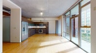 Located at 120 Westlake Avenue in Seattle's South Lake Union neighborhood, this single-floor residence showcases a contemporary industrial-modern aesthetic throughout. Exposed concrete ceilings and polished bamboo flooring create a cohesive design language that extends across the entire space, balancing raw texture with warm, natural tones.

The open-concept living and kitchen area is a standout feature, anchored by expansive floor-to-ceiling windows and a glass-panel door that opens to a private balcony, flooding the space with natural light and offering views of the surrounding Seattle cityscape. The kitchen is well-appointed with dark walnut-toned cabinetry, frosted glass upper cabinet accents, granite countertops, and a full suite of stainless steel appliances including a gas range with oven, built-in microwave, and a side-by-side refrigerator with ice and water dispenser.

The bathroom is finished with large-format tile flooring, dark wood vanity cabinetry, a granite countertop, and an integrated sink. A dedicated laundry area houses a stacked washer and dryer unit, providing practical in-unit convenience. Track lighting and exposed ductwork in the utility corridor add to the space's industrial character, while a prominent exposed concrete wall reinforces the architectural theme throughout.