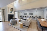 This 1340 square foot single-story space in Cary, NC, showcases a modern and inviting open floor plan. The main living area is anchored by a striking fireplace with a slate surround and white mantel, complemented by abstract art. Light wood flooring runs throughout, enhancing the bright and airy feel.

The space seamlessly integrates multiple functional areas. A comfortable seating arrangement faces the fireplace, ideal for relaxation. The dining area features a wooden table with gray upholstered chairs, perfect for meals or casual gatherings. A mounted TV and additional artwork adorn the walls, adding visual interest.

A standout feature is the stylish bar area, boasting white cabinetry with X-pattern detailing, pendant lighting, and high-backed bar stools. This space is ideal for entertaining or casual dining. The room's design is further elevated by recessed lighting and crown molding.

Additional seating areas with modern furnishings and carefully curated decor pieces create multiple zones for socializing. Large windows and French doors allow natural light to flood the space, while offering views and access to the outdoors. The overall aesthetic is clean, contemporary, and highly functional, making it an ideal setting for both everyday living and hosting events.