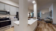 This single-floor residence offers a thoughtfully designed open-concept layout with a cohesive modern aesthetic carried throughout. Wood-look flooring runs continuously across the living, dining, and kitchen areas, contributing to a warm and unified feel. The living room features soaring ceilings, a ceiling fan, and a glass door with transom windows above that invite natural light and provide access to an outdoor balcony area.

The kitchen is equipped with stainless steel appliances, including a range, microwave, and refrigerator, complemented by soft gray shaker-style cabinetry, a herringbone tile backsplash, and light quartz countertops. A peninsula with an integrated sink creates a natural division between the kitchen and the open living space. A dedicated pantry closet and a nearby dining nook with room for a four-seat table complete the culinary zone.

Two bedrooms provide distinct retreats. The primary bedroom features large windows with roller shades, and the secondary bedroom includes a built-in desk area. Both bathrooms echo the kitchen's gray cabinetry and feature wood-look tile flooring. One bath offers a soaking tub and walk-in closet, while the other includes an industrial-style open shelving unit, adding a distinctive design touch.