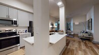 This single-floor residence offers a thoughtfully designed open-concept layout with a cohesive modern aesthetic carried throughout. Wood-look flooring runs continuously across the living, dining, and kitchen areas, contributing to a warm and unified feel. The living room features soaring ceilings, a ceiling fan, and a glass door with transom windows above that invite natural light and provide access to an outdoor balcony area.

The kitchen is equipped with stainless steel appliances, including a range, microwave, and refrigerator, complemented by soft gray shaker-style cabinetry, a herringbone tile backsplash, and light quartz countertops. A peninsula with an integrated sink creates a natural division between the kitchen and the open living space. A dedicated pantry closet and a nearby dining nook with room for a four-seat table complete the culinary zone.

Two bedrooms provide distinct retreats. The primary bedroom features large windows with roller shades, and the secondary bedroom includes a built-in desk area. Both bathrooms echo the kitchen's gray cabinetry and feature wood-look tile flooring. One bath offers a soaking tub and walk-in closet, while the other includes an industrial-style open shelving unit, adding a distinctive design touch.