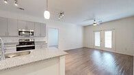 This single-floor, 2-bedroom, 2-bathroom residence offers a thoughtfully designed open-concept layout that maximizes functionality and flow. The kitchen is a standout feature, equipped with stainless steel appliances — including a range, microwave, and refrigerator — complemented by sleek gray cabinetry, granite countertops, and a peninsula with a built-in sink that opens to the living area. Pendant and track lighting illuminate the kitchen, while wood-look flooring extends throughout the main living spaces, adding warmth and cohesion.

The living room is bright and airy, highlighted by a ceiling fan and French doors that invite natural light and provide outdoor access. Both bedrooms are carpeted for comfort, each featuring a ceiling fan, window with blinds, and a dedicated closet. The primary bedroom offers a generous footprint with ample room for furnishings.

The two bathrooms are finished consistently with granite-topped vanities featuring gray cabinetry and wood-look flooring. One bathroom includes a full tub-shower combination with white subway tile surround. The clean, neutral color palette throughout creates a bright, modern ambiance, making this a versatile and move-in ready space.