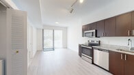 Located at 6043 Southern Blvd in West Palm Beach, Florida, this single-floor residence presents a clean, contemporary design with a thoughtfully arranged open layout. Light-toned hardwood-style flooring runs throughout the main living areas, reflecting natural light and contributing to the bright, airy ambiance of the space.

The kitchen is a standout feature, outfitted with rich dark espresso cabinetry extending to the ceiling for generous storage, granite-style countertops, a classic white subway tile backsplash, and a full suite of stainless steel appliances including a range, microwave, dishwasher, and refrigerator. Track lighting overhead ensures excellent task illumination. The kitchen opens seamlessly into the living area, which benefits from a large sliding glass door fitted with vertical blinds, providing access to outdoor views and abundant natural light.

The bedroom is a tranquil, well-proportioned room with the same light flooring, crisp white walls, and a window overlooking the lush greenery outside, including views of palm trees that reflect the Florida setting.

The bathroom is finished with large-format neutral tile surrounding a full soaking tub and shower combination, complemented by a granite-topped vanity and modern fixtures, delivering a polished and functional space.