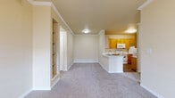 This single-story, 4-bedroom, 1-bathroom home offers a well-organized layout across a comfortable footprint. The combined kitchen and living area forms the heart of the home, featuring an open-concept design with a peninsula countertop finished in light marbled stone, a double stainless steel sink, warm honey-toned wood cabinetry, and wood-look flooring. White appliances including an electric range, microwave, and dishwasher complete the functional kitchen. The adjoining living room is carpeted and benefits from crown molding, a ceiling fan with light fixture, and a glass door that invites natural light. A standout architectural feature is the vaulted ceiling visible in the main living corridor, adding a sense of openness and volume to the space. Built-in open shelving provides a practical storage and display element. The four bedrooms are carpeted and bright, with windows fitted with horizontal blinds allowing natural light. The primary bedroom offers a generous footprint suitable for a full suite setup. Additional spaces include a dedicated laundry area with washer and dryer hookups and wood-look flooring, two closets, and a connecting hallway. Neutral warm-beige walls and light carpet throughout create a cohesive and inviting atmosphere.