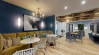 Located at 9005 Oak Village Blvd in Lewis Center, Ohio, this thoughtfully designed single-floor clubhouse offers a welcoming and upscale communal environment. The space is anchored by a comfortable lounge area featuring a striking floor-to-ceiling tiled fireplace, coffered ceilings with exposed wood beams, a globe chandelier, and large windows dressed in bold patterned drapery that allow generous natural light to fill the room. Plush seating in navy and neutral tones surrounds a live-edge wood coffee table, creating an inviting gathering space.

Adjacent to the lounge is a stylish café-style seating area with deep teal shiplap accent walls, a statement multi-bulb chandelier, and a tufted olive green banquette complemented by marble-top tables and woven accent chairs. Curated artwork and sleek wall sconces add to the refined aesthetic throughout.

The fully equipped kitchen is outfitted with rich forest green cabinetry, brass hardware, white quartz countertops, a marble tile backsplash, and stainless steel appliances, including a full-size refrigerator. Pendant lighting and a built-in bar ledge with exterior views complete this functional yet elegant space.

The entry area features textured wallcovering, herringbone-patterned flooring, and branded mission statement signage, setting a purposeful and polished tone from arrival. Light wood-look flooring flows consistently throughout the entire space, unifying the design.