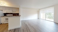 Suite 4-421 is a well-appointed single-floor residence that combines a clean, neutral aesthetic with functional design throughout. Light wood-style plank flooring extends continuously across the main living areas, creating a cohesive and easy-to-maintain foundation. The open-concept living and dining area is generously proportioned, with crisp white walls, sliding glass door access to a private balcony, and a window that draws in natural light. A peninsula counter with dark granite surfaces separates the living space from the kitchen, which is fully equipped with white cabinetry, dark granite countertops, a tile backsplash, and a full suite of white appliances including a refrigerator, electric range, over-range microwave, and sink. The bedroom is a spacious, light-filled room with a large window offering exterior views and ample floor space. A pendant light fixture in the main area adds a decorative touch. The bathroom is finished with tile flooring, a white vanity with a granite countertop, and a tub-shower combination enclosed by sliding glass doors with a tiled accent border. Louvered closet doors and HVAC vents throughout complete the practical details of this clean, move-in-ready suite.