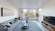 This single-floor residence offers a thoughtfully designed layout with two bedrooms and two bathrooms, finished in a clean, modern aesthetic throughout. Light wood-style flooring runs continuously across the space, complementing the bright white walls and creating a cohesive, airy atmosphere.

The living area is a standout feature, anchored by a large multi-pane window that frames outdoor tree views and fills the room with abundant natural light. The open-concept design connects the living space to a dedicated dining area, making it well-suited for everyday living and entertaining.

The kitchen is outfitted with two-tone cabinetry — dark upper cabinets paired with glossy grey lower cabinets — set against clean white countertops. Stainless steel appliances, including a gas range, microwave, dishwasher, and refrigerator, complete the functional workspace.

Both bedrooms are generously proportioned and well-lit. One bedroom features tall windows with neighborhood views, while the other includes closet storage. Each bathroom is finished with dark vanity cabinetry, white countertops, and light wood-style flooring, maintaining the consistent modern palette found throughout the residence.
