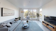 This single-floor residence offers a thoughtfully designed layout with two bedrooms and two bathrooms, finished in a clean, modern aesthetic throughout. Light wood-style flooring runs continuously across the space, complementing the bright white walls and creating a cohesive, airy atmosphere.

The living area is a standout feature, anchored by a large multi-pane window that frames outdoor tree views and fills the room with abundant natural light. The open-concept design connects the living space to a dedicated dining area, making it well-suited for everyday living and entertaining.

The kitchen is outfitted with two-tone cabinetry — dark upper cabinets paired with glossy grey lower cabinets — set against clean white countertops. Stainless steel appliances, including a gas range, microwave, dishwasher, and refrigerator, complete the functional workspace.

Both bedrooms are generously proportioned and well-lit. One bedroom features tall windows with neighborhood views, while the other includes closet storage. Each bathroom is finished with dark vanity cabinetry, white countertops, and light wood-style flooring, maintaining the consistent modern palette found throughout the residence.