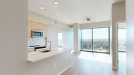 Located in the heart of Raleigh, NC, this modern residence offers six bedrooms and two bathrooms across a single thoughtfully designed floor. The open-concept living and kitchen area immediately impresses with floor-to-ceiling glass walls and sliding balcony doors that flood the space with natural light and frame breathtaking panoramic views of the Raleigh skyline and surrounding greenery. Light-toned hardwood flooring runs throughout, enhancing the bright, airy ambiance.

The contemporary kitchen features flat-front light wood cabinetry, a classic white subway tile backsplash, stainless steel appliances including a refrigerator, electric range, and microwave, and a generous quartz-topped island with an undermount sink — ideal for both cooking and casual dining.

The bedrooms are well-proportioned, with the primary bedroom boasting corner floor-to-ceiling windows that offer stunning elevated city views. The bathrooms are finished in a clean, modern style, with dual-sink vanities, light wood cabinetry, and glass-enclosed showers. A dedicated laundry area houses a stacked washer and dryer unit with built-in shelving. A ceiling fan in the living area and additional closet space complete this well-appointed, light-filled residence.