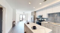 Located at 1777 Peachtree Rd NW in Atlanta's vibrant Buckhead/Midtown corridor, this well-appointed one-bedroom, one-bathroom residence offers a thoughtfully designed open-concept layout. The modern kitchen is a standout, featuring two-tone cabinetry with white upper cabinets and wood-grain lower cabinets, a quartz waterfall island perfect for dining or entertaining, a subway tile backsplash, stainless steel appliances including a French door refrigerator, electric range, microwave, and dishwasher. The kitchen flows seamlessly into the living area, which is bathed in natural light and opens to a private balcony through sliding glass doors, offering sweeping views of the Atlanta skyline. The bedroom is carpeted for comfort, fitted with a ceiling fan, and features a large window framing additional city views. The bathroom includes warm wood-tone LVP flooring, a vanity with storage, and a tub/shower combination. A dedicated laundry area with an in-unit top-load washer adds everyday convenience. Recessed lighting, dark hardwood-style flooring in the main living areas, and clean white walls contribute to the space's bright, contemporary ambiance throughout.