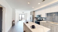 Located at 1777 Peachtree Rd NW in Atlanta's vibrant Buckhead/Midtown corridor, this well-appointed one-bedroom, one-bathroom residence offers a thoughtfully designed open-concept layout. The modern kitchen is a standout, featuring two-tone cabinetry with white upper cabinets and wood-grain lower cabinets, a quartz waterfall island perfect for dining or entertaining, a subway tile backsplash, stainless steel appliances including a French door refrigerator, electric range, microwave, and dishwasher. The kitchen flows seamlessly into the living area, which is bathed in natural light and opens to a private balcony through sliding glass doors, offering sweeping views of the Atlanta skyline. The bedroom is carpeted for comfort, fitted with a ceiling fan, and features a large window framing additional city views. The bathroom includes warm wood-tone LVP flooring, a vanity with storage, and a tub/shower combination. A dedicated laundry area with an in-unit top-load washer adds everyday convenience. Recessed lighting, dark hardwood-style flooring in the main living areas, and clean white walls contribute to the space's bright, contemporary ambiance throughout.