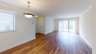 Located at 5114 Dudley Ln in Bethesda, Maryland, this single-floor residence offers a well-organized and functional layout throughout. The spacious living and dining area is highlighted by rich hardwood flooring, crown molding details, and a pendant light fixture that anchors the space. A large sliding glass door floods the room with natural light and provides outdoor access, while a pass-through window connects seamlessly to the kitchen. The galley-style kitchen is equipped with warm wood cabinetry, dark granite-style countertops, tile backsplash, and black appliances including a refrigerator, range, and dishwasher, all set atop durable hardwood-style flooring. The bedrooms feature neutral-toned carpeting, natural light from windows with blinds, and closets with classic six-panel doors, offering comfortable and quiet retreats. One bedroom includes direct access to a full bathroom, providing added convenience. The bathrooms are finished with warm tile surrounds featuring decorative accent borders on the tub-shower combinations, wood vanities with white countertops, and well-lit mirrors. The overall palette of soft whites and warm neutrals throughout creates a clean, inviting atmosphere well-suited for comfortable everyday living.
