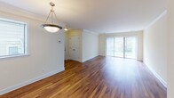 Located at 5114 Dudley Ln in Bethesda, Maryland, this single-floor residence offers a well-organized and functional layout throughout. The spacious living and dining area is highlighted by rich hardwood flooring, crown molding details, and a pendant light fixture that anchors the space. A large sliding glass door floods the room with natural light and provides outdoor access, while a pass-through window connects seamlessly to the kitchen. The galley-style kitchen is equipped with warm wood cabinetry, dark granite-style countertops, tile backsplash, and black appliances including a refrigerator, range, and dishwasher, all set atop durable hardwood-style flooring. The bedrooms feature neutral-toned carpeting, natural light from windows with blinds, and closets with classic six-panel doors, offering comfortable and quiet retreats. One bedroom includes direct access to a full bathroom, providing added convenience. The bathrooms are finished with warm tile surrounds featuring decorative accent borders on the tub-shower combinations, wood vanities with white countertops, and well-lit mirrors. The overall palette of soft whites and warm neutrals throughout creates a clean, inviting atmosphere well-suited for comfortable everyday living.