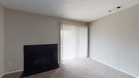 This single-floor residence offers a practical and comfortable layout with several functional living spaces. The living room serves as a central gathering area, anchored by a dark tile-surround fireplace and a large sliding glass door fitted with vertical blinds, allowing natural light to filter throughout the space. The living area features a combination of durable wood-style flooring and plush carpeting, creating defined zones within the open layout.

The kitchen is efficiently designed in a U-shaped configuration, featuring gray cabinetry with ample upper and lower storage, light speckled countertops, a breakfast bar peninsula, and wood-style flooring. White appliances, including a range, microwave, and refrigerator, are included. The kitchen opens toward the dining and living areas, promoting an easy flow between spaces.

The bedroom is a well-proportioned carpeted room equipped with a ceiling fan with integrated lighting, providing comfort and ventilation. The bathroom includes a speckled countertop vanity with an undermount sink, a large mirror, and a textured wall finish, maintaining a clean and functional aesthetic throughout. Textured ceilings are present across the unit.