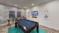 This single-floor amenity space is thoughtfully designed with a cohesive contemporary aesthetic, blending bold textures, rich finishes, and curated décor across several distinct functional areas.

The game room serves as a central gathering point, anchored by a full-size pool table with blue felt set atop a vibrant teal area rug. Herringbone-patterned flooring runs throughout, lending a refined visual continuity to the space. A wall-mounted flat-screen television and stylish framed artwork complete the room, while a striking bird-motif wallcovering adds a bold decorative accent.

Adjacent to the game room is a well-appointed wet bar area featuring a generous white quartz countertop with under-counter illumination, dark wood cabinetry, a beverage refrigerator, and open floating shelves adorned with decorative objects. Blue herringbone tile forms a dramatic backsplash behind the shelving.

The lounge area offers a more intimate atmosphere, with teal-toned wall paneling, plush seating, a wall-mounted television, large windows that invite natural light and outdoor views, and a sculptural branching chandelier overhead.

A dedicated business center provides workstations with computers and a printer, accented by the same teal wall paneling and chandelier design, creating a consistent and polished environment suited for productivity.