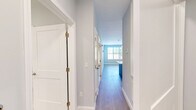 This well-appointed unit in Swanzey, NH offers a thoughtfully designed single-floor layout with one bedroom, a versatile den, and one full bathroom. The open-concept living and kitchen area creates a welcoming, airy atmosphere anchored by light wood-look flooring and soft blue-gray walls that carry consistently throughout the home. The modern kitchen is a standout feature, showcasing crisp white cabinetry, a subway tile backsplash, quartz countertops, a central island with pendant lighting, and a full suite of stainless steel appliances including a range, over-the-range microwave, dishwasher, and refrigerator. The living room is bright and open, with large windows that invite natural light and offer views of the surrounding neighborhood. The primary bedroom is generously sized, featuring a wide window with outdoor views and ample room for furnishings. The den provides flexible additional space ideal for a home office or guest room, also benefiting from natural light. The full bathroom features marble-look tile flooring, a soaking tub with shower, and clean, contemporary finishes. A dedicated closet adds practical storage. The wide, well-lit hallway connects all rooms seamlessly, reinforcing the unit's clean and modern aesthetic.