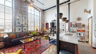 Located at 1101 Hawthorne Lane in Charlotte's vibrant Plaza Midwood neighborhood, this one-bedroom, one-bathroom loft showcases an impressive industrial-chic aesthetic rooted in its converted warehouse origins. The open-plan living area commands attention with soaring ceilings, exposed brick walls, and a dramatic arched window that floods the space with abundant natural light. Polished concrete floors run throughout, complementing the raw architectural character. The kitchen features granite countertops and a breakfast bar with seating, seamlessly connecting to the living area. The spacious bedroom continues the loft's bold design language, with exposed brick, floor-to-ceiling steel-framed windows, and direct access to a private outdoor patio — an uncommon amenity that provides a serene retreat within the urban setting. The patio itself is framed by the original brick walls of the surrounding building, offering a sheltered and intimate outdoor space. The bathroom is richly appointed with a granite vanity, dark cabinetry, decorative wall-to-ceiling gallery arrangements, and warm sconce lighting that creates an atmospheric, boutique-hotel feel. Throughout the space, high ceilings and large industrial-style windows reinforce a sense of openness and volume that far exceeds the physical footprint of this thoughtfully designed urban loft.