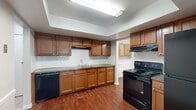 Located at 4285 Chestnut Ridge Rd in Amherst, NY, this single-floor home offers four bedrooms, three bathrooms, and a practical, well-organized layout. The kitchen is a functional centerpiece, featuring warm medium-tone wood cabinetry, dark granite-style countertops, a double sink, and black appliances including a range, dishwasher, and refrigerator. A raised tray ceiling with a skylight-style fixture adds architectural interest and brightens the space. Rich hardwood-style flooring flows through the kitchen and connecting hallways, creating a cohesive, polished look. The living area is generously sized, with neutral carpet, a ceiling fan, and large windows that bring in natural light. The four bedrooms are carpeted and finished in soft neutral tones, providing a calm and comfortable atmosphere; the spacious primary bedroom includes walk-in closet space with built-in shelving and hanging rods. The three bathrooms are clean and functional, featuring white tile wainscoting, natural light from windows with blinds, and walk-in shower enclosures. Throughout the home, consistent neutral gray walls, white trim, and a mix of carpet and hardwood-style flooring create a cohesive and move-in-ready environment.
