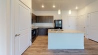 This well-appointed single-floor residence offers a thoughtfully designed open-concept layout that seamlessly connects the kitchen and living areas. The kitchen is a standout feature, showcasing dark espresso cabinetry, granite-style countertops, a large central island with pendant lighting overhead, and a full suite of black appliances including a refrigerator, range, microwave, and dishwasher. Light wood-tone flooring runs throughout the main living areas, complementing the crisp white walls and creating a bright, welcoming atmosphere. Track lighting in the living area adds a modern touch, while the open floor plan provides generous, flexible living space.

The two bedrooms are carpeted for comfort and feature large windows that invite natural light and offer views of the surrounding greenery. Each bedroom includes access to a closet, with one room featuring a walk-in closet. The two bathrooms are finished consistently with the rest of the home, featuring dark wood vanities topped with granite-style countertops, undermount sinks, and wood-tone flooring. One bathroom includes a full tub-shower combination. Clean white walls and recessed lighting complete each bathroom's clean, contemporary aesthetic. Overall, this residence delivers a cohesive modern design with practical, quality finishes throughout.