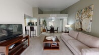 This single-floor residence offers a thoughtfully designed open-concept layout that seamlessly connects the living, dining, and kitchen areas. The living room features plush carpeting, vaulted ceilings with a ceiling fan, a corner fireplace, and sliding glass doors that fill the space with natural light and provide access to an outdoor balcony. The adjacent dining area accommodates a full dining set and flows naturally into the kitchen. The kitchen is well-equipped with black appliances including a gas range, microwave, dishwasher, and refrigerator, complemented by light wood cabinetry, light countertops, and durable hardwood-style flooring. A dedicated walk-in pantry provides generous storage. The bedroom features vaulted ceilings, a ceiling fan, plush carpeting, a window with draping, and access to a spacious walk-in closet. Two bathrooms are present, each with light wood vanity cabinetry, wide mirrors, and tiled shower-tub combinations. The in-unit laundry room includes a full-size washer and dryer, hardwood-style flooring, overhead cabinetry, and built-in shelving for additional storage. Neutral tones and consistent finishes throughout lend the space a cohesive and comfortable ambiance.