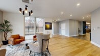 Located at 857A Federal Rd in Brookfield, CT, this generously sized single-floor amenity space offers a thoughtfully designed environment built for both relaxation and social engagement. The layout flows seamlessly across several distinct functional zones, each finished with contemporary style and attention to detail.

The main lounge area features polished concrete flooring, a coffered tray ceiling with warm ambient uplighting, and a striking cluster of globe pendant lights. A large quartz-topped kitchen island anchors the entertaining zone, complemented by deep navy cabinetry, a tile backsplash, and stainless steel appliances. A full-size pool table serves as a centerpiece for the game area, surrounded by plush sectional seating and vibrant accent furnishings.

A bright, airy reception lounge showcases wide-plank hardwood flooring, floor-to-ceiling windows overlooking the outdoors, and a modern chandelier. This area transitions into a welcoming seating zone with stylish wingback chairs and curated artwork on the walls. A decorative room divider with built-in display shelving and a mounted flat-screen TV adds architectural character.

Additional areas include a fitness zone and private rooms accessible via glass-paned French doors. Throughout, recessed lighting, neutral gray tones, and bold navy accents create a cohesive, upscale ambiance ideal for community gathering and everyday amenity use.