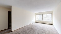 Located at 333 Oak Grove St in Minneapolis, MN, this one-bedroom, one-bathroom unit offers a practical and straightforward layout across a single floor. The living area is generously proportioned, featuring wall-to-wall carpeting, neutral cream-toned walls, a textured ceiling, and a wide multi-pane window that invites natural light and outdoor views of the surrounding greenery. A baseboard heating system runs along the exterior wall, ensuring efficient climate control. The kitchen is positioned adjacent to the living space and includes a stove and sink set within a compact, functional layout with tile flooring. The bedroom is a comfortable size, also carpeted, and features a window with an integrated wall air conditioning unit, as well as a built-in closet with louvered bifold doors offering ample storage with shelving and hanging space. The hallway connects the main living areas to the full bathroom, which includes a tiled tub/shower combination, toilet, and vanity with classic small-format tile flooring. Dark wood-toned doors throughout add a consistent design element. This unit provides a clean, functional living space in a well-situated Minneapolis location.