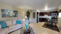This single-floor residence is thoughtfully designed with a cohesive, neutral color palette accented by teal throughout. The open-concept living area flows seamlessly into the kitchen, with large-format light tile flooring unifying the space. The living room offers generous seating space, accommodating a sectional sofa arrangement, glass coffee table, and decorative accents, creating a comfortable and welcoming atmosphere.

The kitchen is well-equipped with rich dark espresso cabinetry extending to the ceiling, granite countertops, a tile backsplash, and a full suite of stainless steel appliances including a refrigerator, range, microwave, and dishwasher. A compact dining area adjacent to the kitchen includes a window for natural light.

The primary bedroom features plush carpeting, a ceiling fan, sliding glass doors allowing natural light, and ample wall space. A second carpeted bedroom, also with a ceiling fan and window, provides flexibility as a guest room or home office.

The bathroom is finished with a dark vanity topped with granite, a large mirror, tile flooring, and a tub-shower combination with tile surround, maintaining the consistent design aesthetic found throughout the residence.
