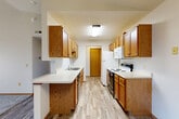 Located at 6500 W 43rd St in Sioux Falls, SD, this 2-bedroom, 2-bathroom unit offers a well-organized, single-floor layout with a functional and comfortable design throughout. The galley-style kitchen is a standout feature, lined on both sides with warm oak cabinetry offering ample upper and lower storage, white appliances including a range, refrigerator, microwave, and dishwasher, along with a double-basin sink and generous counter space with a peninsula that opens toward the main living area. Light wood-look flooring runs through the kitchen and hallways, providing a clean, cohesive look. The living area features vaulted ceilings, a textured ceiling finish, and a large sliding glass door that fills the space with natural light and leads out to a private balcony with outdoor views. Both bedrooms are carpeted and offer a quiet, comfortable retreat, with the primary bedroom featuring a spacious walk-in closet outfitted with built-in shelving and hanging rods. The two bathrooms are well-appointed; one includes a full tub/shower combo with grab bars and wood-toned vanity, while the second features a bright vanity with a large mirror and abundant drawer storage. Baseboard heating is present throughout, and textured ceilings are consistent across the unit.
