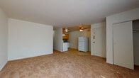 This single-floor unit offers a practical and straightforward layout designed for comfortable everyday living. The open living area is finished with neutral-toned wall-to-wall carpeting that extends throughout most of the unit, lending a cohesive and warm feel to the space. A ceiling fan overhead provides additional air circulation, complementing the window-mounted air conditioning units and baseboard heating found in the individual rooms, ensuring year-round climate control. Natural light enters through windows fitted with blinds and vertical window treatments, brightening the interior.

The kitchen is equipped with warm-toned wood cabinetry offering ample storage, a textured tile backsplash, granite-style countertops, and white appliances including an electric range, dishwasher, and refrigerator. The tile flooring in the kitchen provides a clean contrast to the carpeted living spaces.

The bedrooms are well-proportioned, each featuring carpeted floors, neutral walls, and windows that allow natural light in. The bathroom includes a full soaking tub with a built-in niche, chrome fixtures, and tile-accented walls. A closet near the entry provides additional storage. The unit's layout, visible in the 3D model, reflects an efficient use of space throughout.